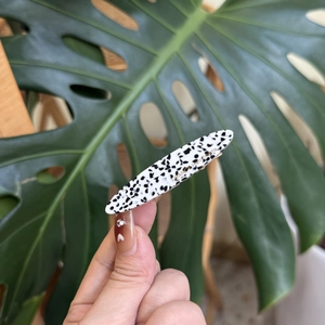 Gros plan sur une pince à cheveux en acétate blanc avec taches noires et lettrage doré