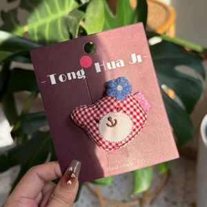 Handmade red checkered bear hair clip with blue crochet flower on card packaging