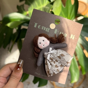 Detailed view of a handmade fabric doll hair clip in Mori girl style on a brown card