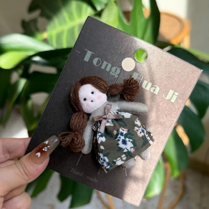 Detail of a handmade doll clip with brown braids and green floral dress on display card