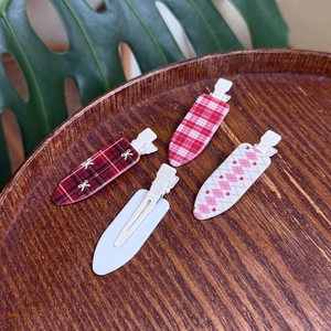Detail of four plaid duckbill hair clips with red tartan and heart patterns on wood