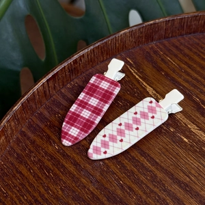 Red plaid and heart argyle pattern hair clips on a wooden tray with green leaves