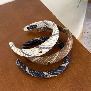Three striped headbands in cream, brown and navy with gold heart charms on wood surface