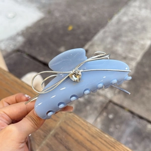 Close-up of sky blue claw clip with silver ribbon bow and heart crystal detail