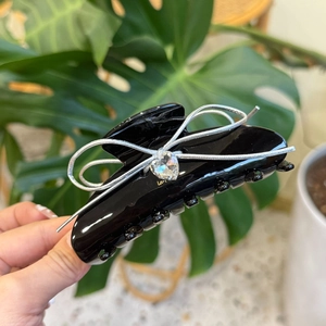 Detailed macro view of black acetate hair claw with a crystal heart and woven ribbon bow