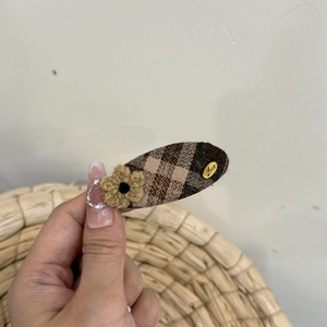Close-up of retro plaid fabric hair clip featuring a beige crochet flower and Love charm