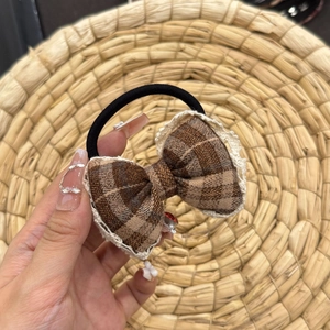 Detail of a brown plaid hair scrunchie with lace edges and a vintage bow design