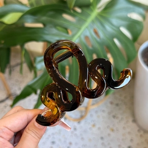 Détail d'une pince à cheveux ambrée translucide avec motif ondulé sur fond de plantes