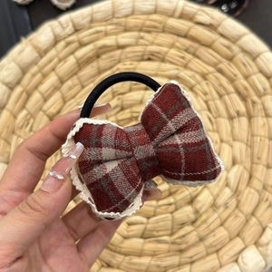 Detail of red plaid scrunchie with white lace trim held against a woven background