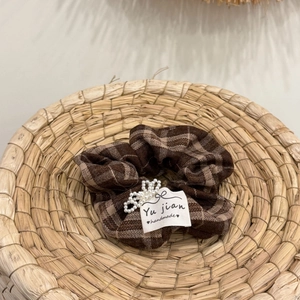 Close-up of brown plaid hair scrunchie with white pearl beads and handmade fabric label