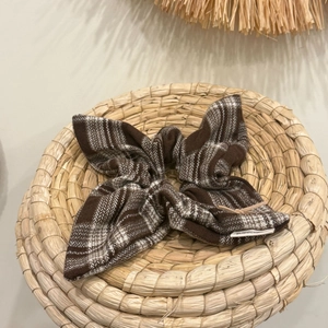 Brown and white plaid fabric hair scrunchie with bow shape on a woven tray