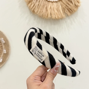 Detalle de una diadema de punto con rayas anchas blancas y negras y etiqueta de oso