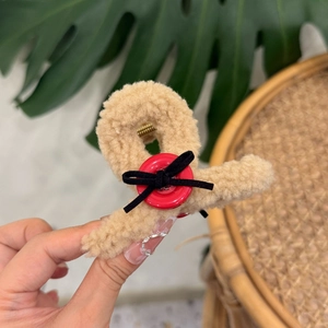 Detail showing plush beige fleece hair claw clip with red button and black bow decoration