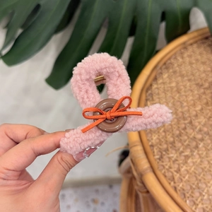 Detail of pink plush teddy hair claw clip featuring a brown button and orange bow decoration