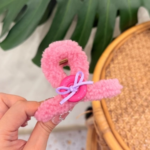 Close-up of bright pink plush teddy hair claw clip with button and purple bow detail
