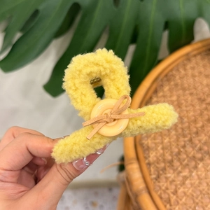 Yellow faux shearling hair claw clip with button and bow detail shown on hand