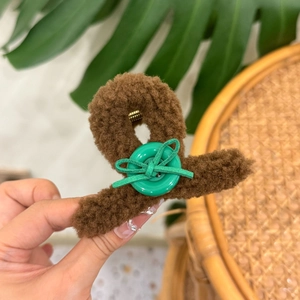 Detail of plush brown shark clip with green button and bow accent on soft teddy fur