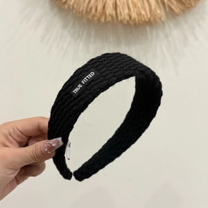 Nahaufnahme des schwarzen Strickstirnbands mit Strukturmuster und True Fitted Textiletikett