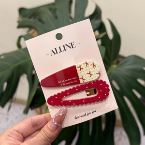 Détail de pinces à cheveux rouges à carreaux et à pois sur une carte rose Alline