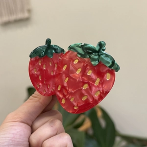 Détail d'une pince à cheveux fraise en résine marbrée avec des paillettes dorées brillantes