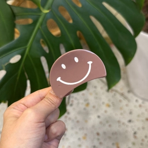 Pince à cheveux marron en acétate avec motif smiley blanc tenue à la main