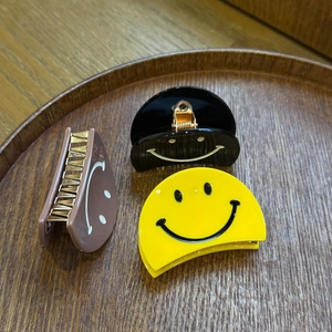 Détail de trois pinces à cheveux smiley en jaune, noir et rose sur un plateau en bois