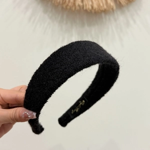 Detail of black felt texture headband with golden brand logo on inner side