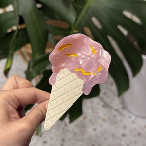 Close-up of pink ice cream cone hair claw clip held by hand against green leaves