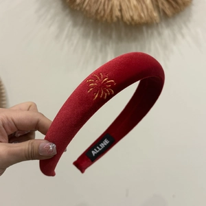 Detail of red velvet headband with gold sunburst embroidery and woven brand label