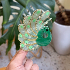 Detailed close-up of a peacock acetate hair claw clip with rhinestones and gold accents