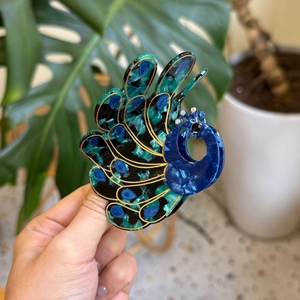 Detail of peacock acetate hair claw clip with golden outlines and crystal accents