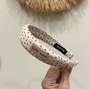 Détail d'un serre-tête rembourré crème à pois rouges avec étiquette de marque cousue