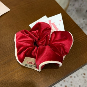 Détail d'un chouchou en velours rouge avec bordure beige et étiquette de logo