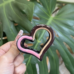 Close-up of heart shaped hair claw clip with colorful resin stripes held by hand