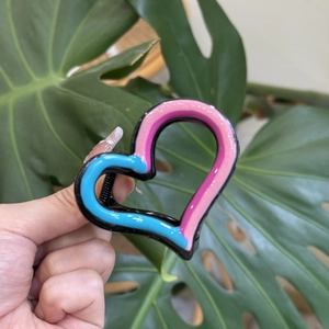 Detail view of heart-shaped hair claw clip in pink and blue enamel finish with metal spring