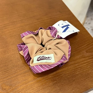 Gros plan détaillé d'un chouchou en tissu double couche à rayures mauves et kaki avec étiquette
