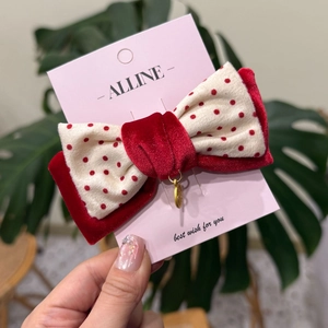 Détail d'une pince à cheveux avec nœud en velours rouge à pois et breloque dorée