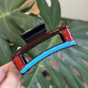 Detail of a wavy resin hair claw clip with colorful block patterns held against leaves