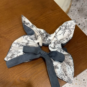Elegant vintage-style bow hair scrunchie with grey floral pattern on wooden background