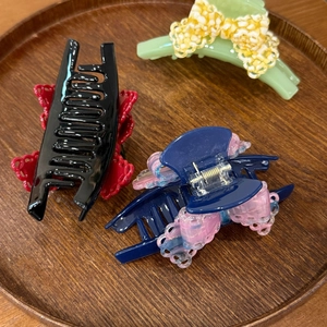 Three acetate hair claws with lace bow details and floral accents on a round wooden tray