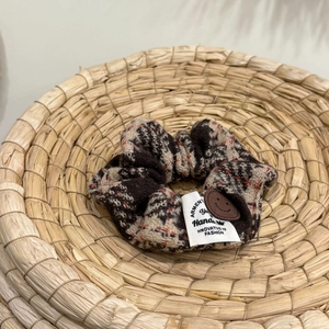 Close-up of brown plaid tweed scrunchie with smiley leather patch on woven tray