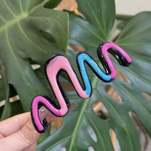 Detail of a wavy resin hair claw clip with pink and blue contrast colors held in hand
