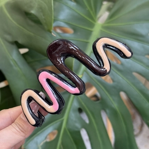Macro shot of wave-shaped hair claw clip featuring colorful drip oil collage patterns