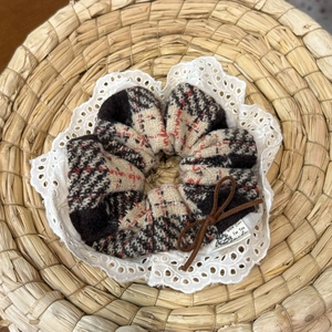 Detail of plaid scrunchie with lace trim, velvet bow, and handmade label on woven mat