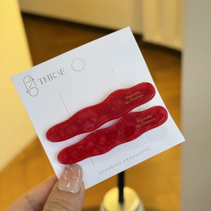 Détail de barrettes à cheveux ondulées rouges en acétate avec logo doré sur carte