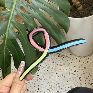 Detail view of a large wave-shaped colorful shark hair claw clip held by hand