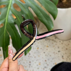 Detail of a wavy resin hair claw clip with pink and beige color-block stripes in hand