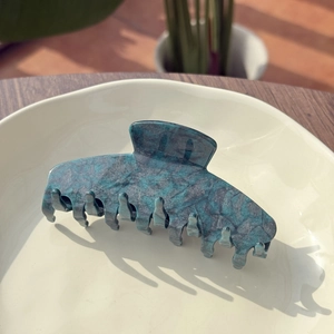 Detail of dark teal marble texture hair claw clip on a cream ceramic plate
