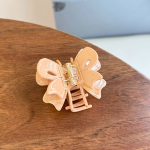 Detail of a creamy peach acetate butterfly hair claw clip with marble texture and gold spring