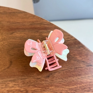 Detailed close-up of pink layered butterfly hair claw clip on dark wood background